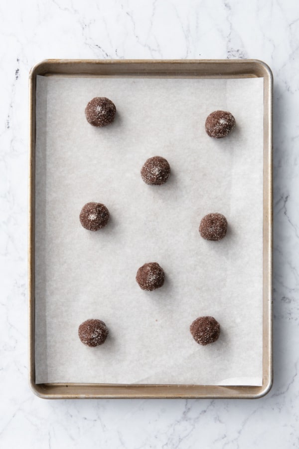 Unbaked sugar-coated cookie dough balls arranged on a parchment-lined baking sheet.