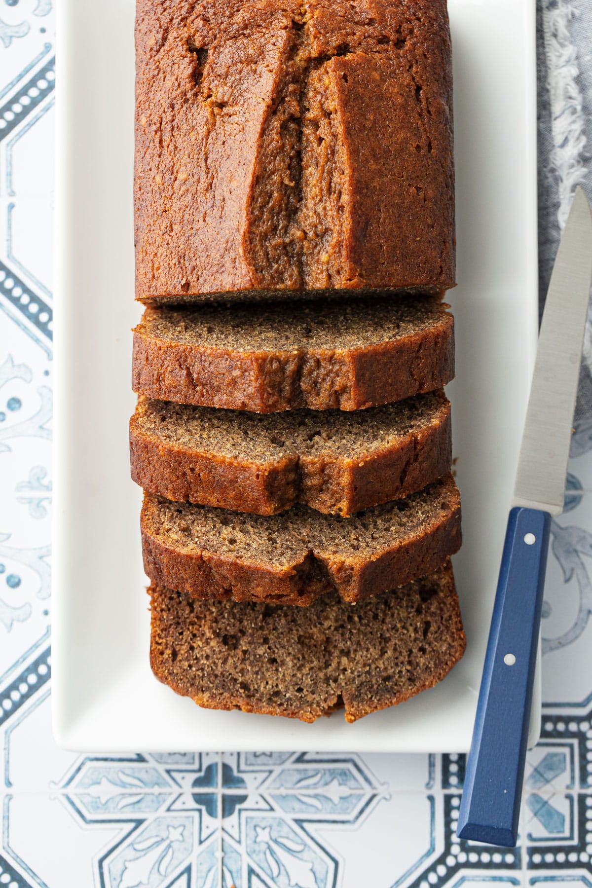 Slices of Spiced Persimmon Bread on a rectangular cake plate with blue knife and a blue and white tile background.