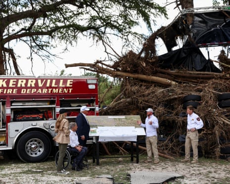 Debris from the flooding can be seen towering above first responders as they brief Trump and Abbott.