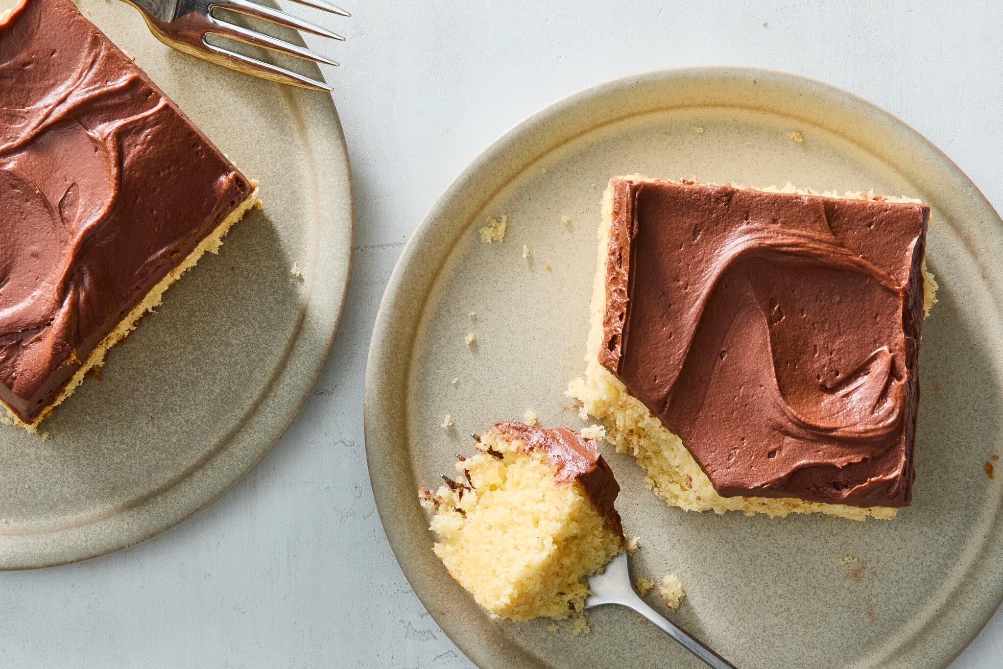 An overhead image of two squares of chocolate-frosted yellow cake.