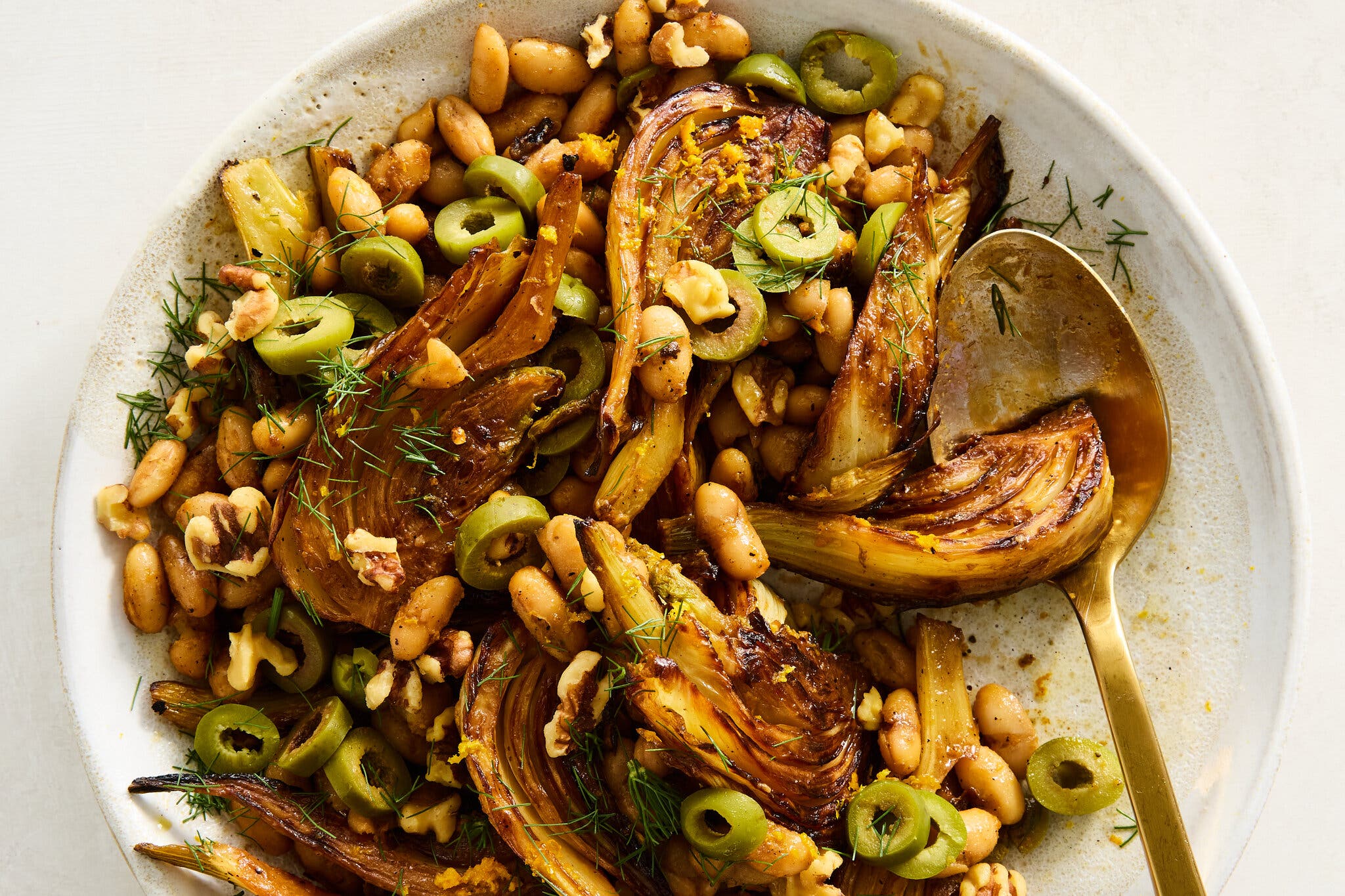 A white stone plate holds caramelized fennel, olives and white beans.
