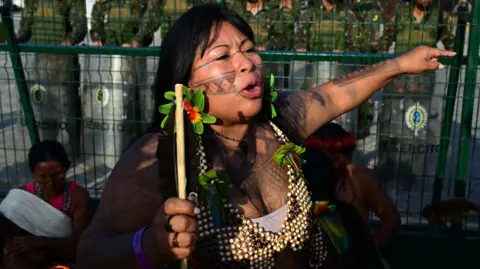 Getty Images An indigenous woman protests in front of a line of soldiers. 
