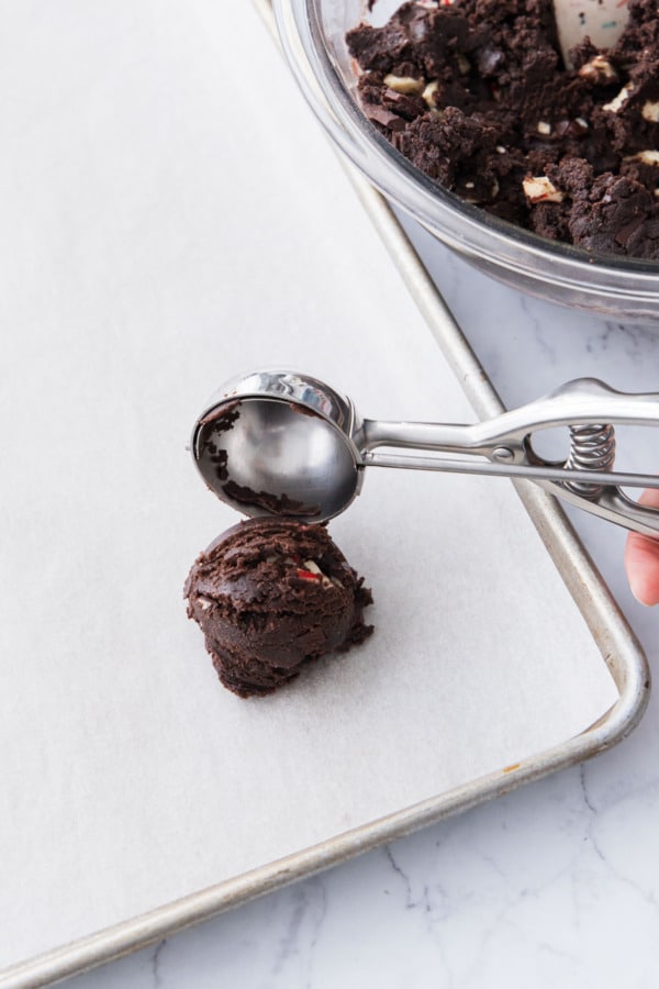 Scoop releasing a ball of chocolate dough onto a parchment lined baking sheet.