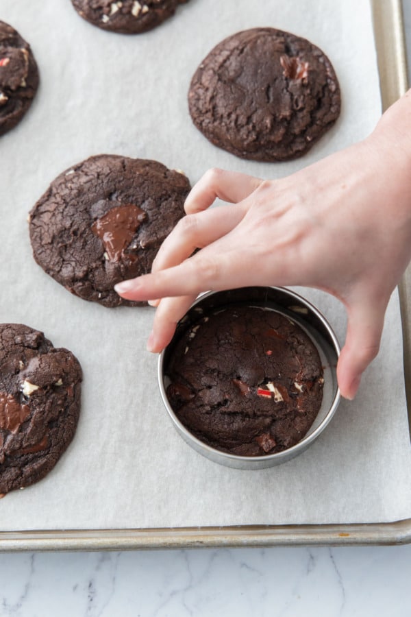 Swirling a round cookie cutter around the cookies just out of the oven to perfect the round shape.