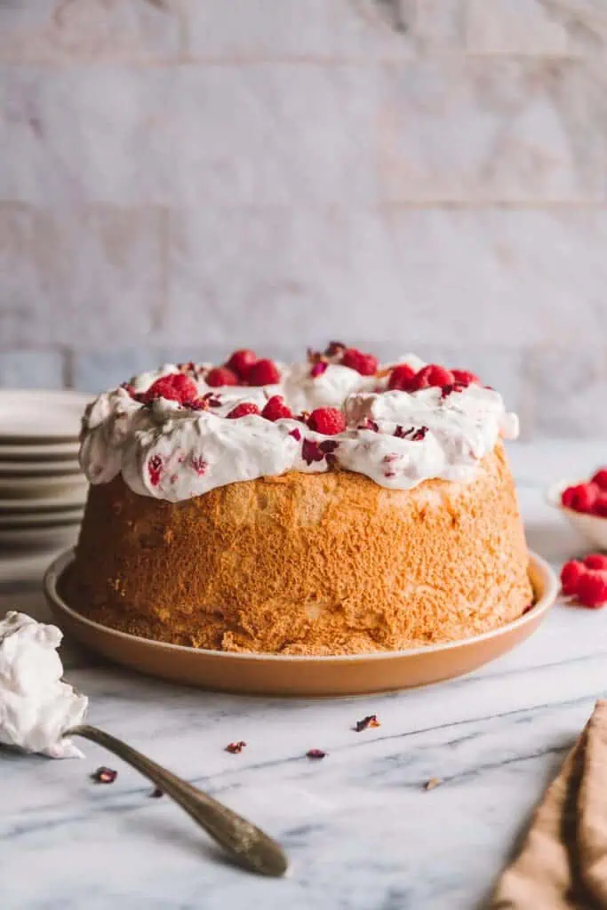 a table with a finished angel food cake recipe, raspberries and plates