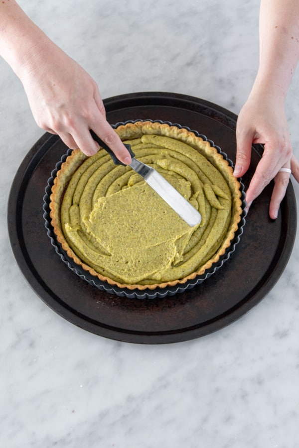 Spreading piped frangipane filling into an even layer in the crust.
